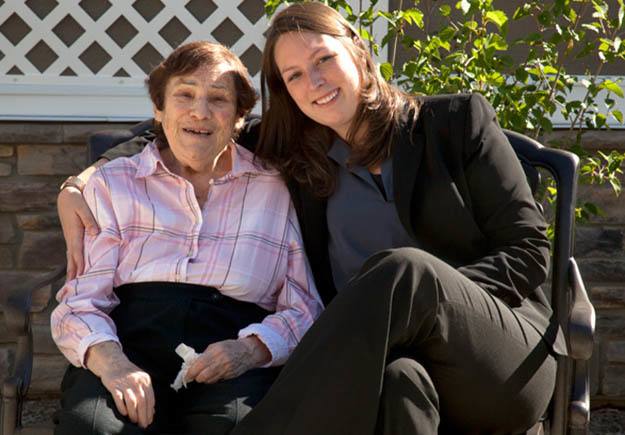 A female resident and an aide sitting on a bench hugging
