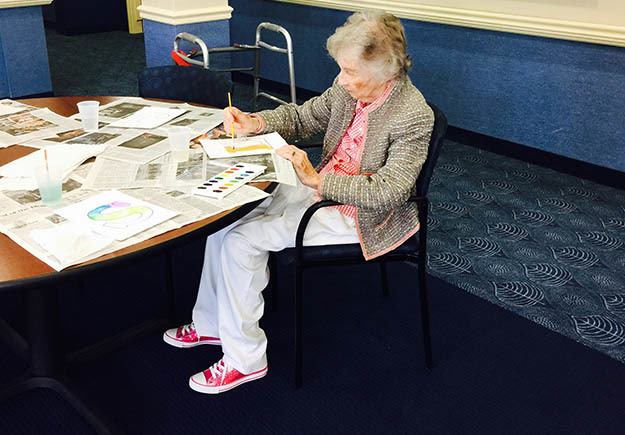 A female resident sitting at the table painting a picture